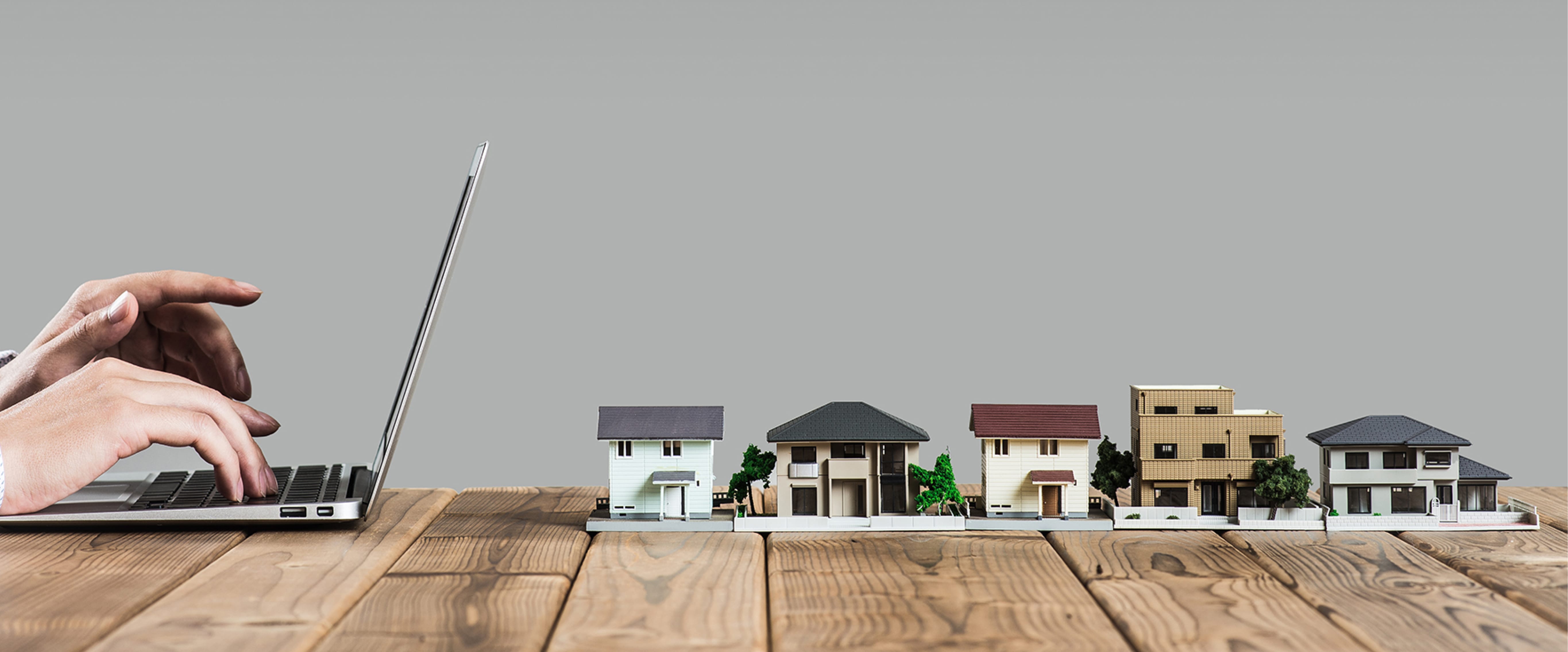 ノートパソコンにタイピングする手と、机の上に並ぶ住宅模型が写っている写真。